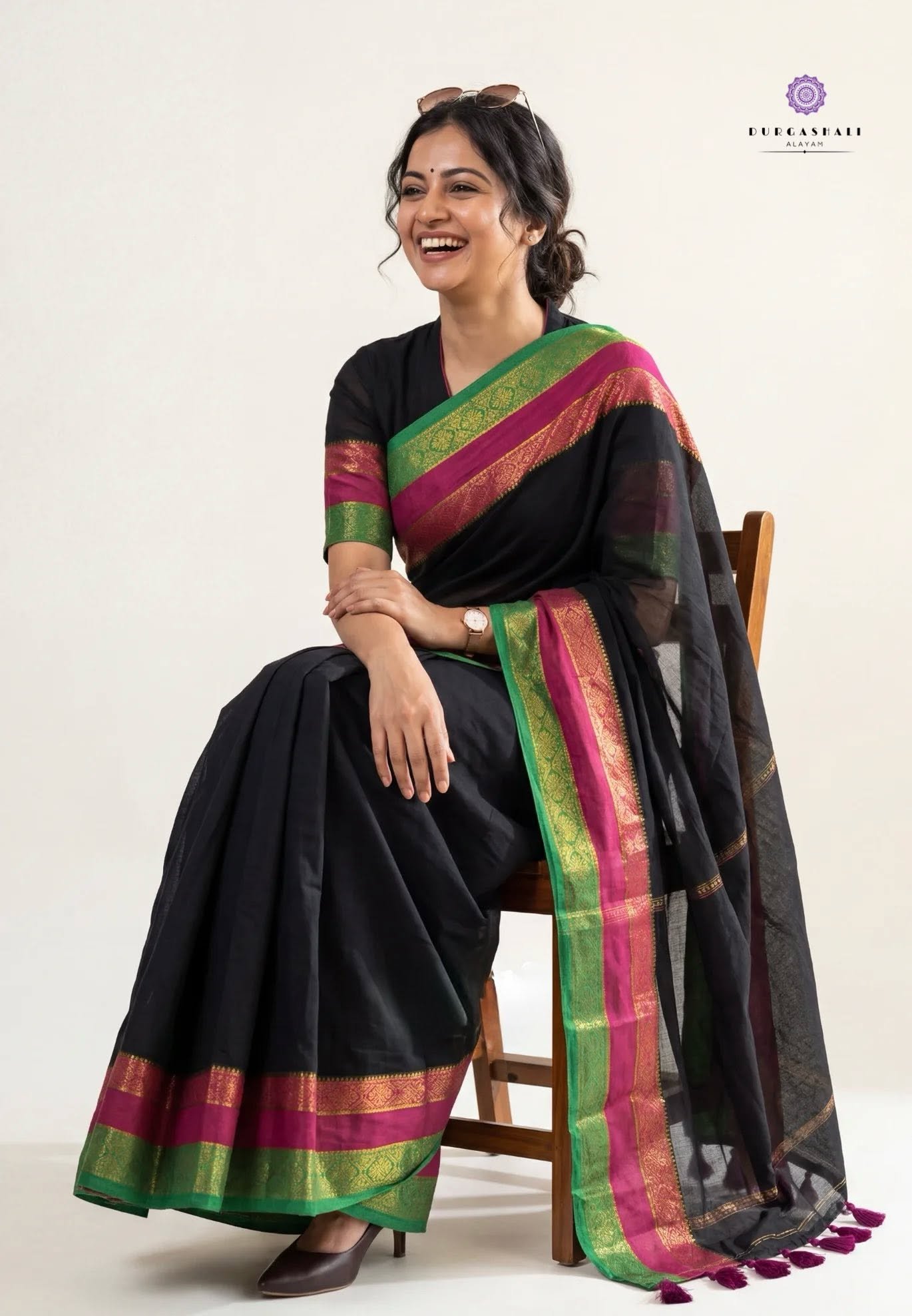 Black saree with green and pink borders on a seated model